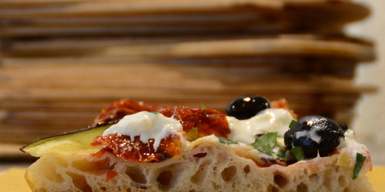 Un trancio di pizza con olive nere, zucchine, stracciatella e pomodorri secchi
